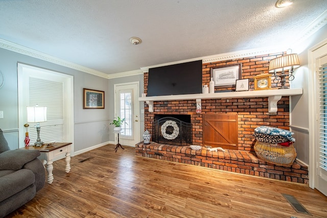 living room featuring wood-type flooring, a brick fireplace, ornamental molding, and a textured ceiling