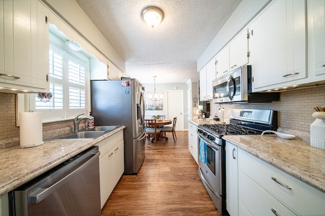 kitchen with sink, appliances with stainless steel finishes, pendant lighting, hardwood / wood-style floors, and white cabinets