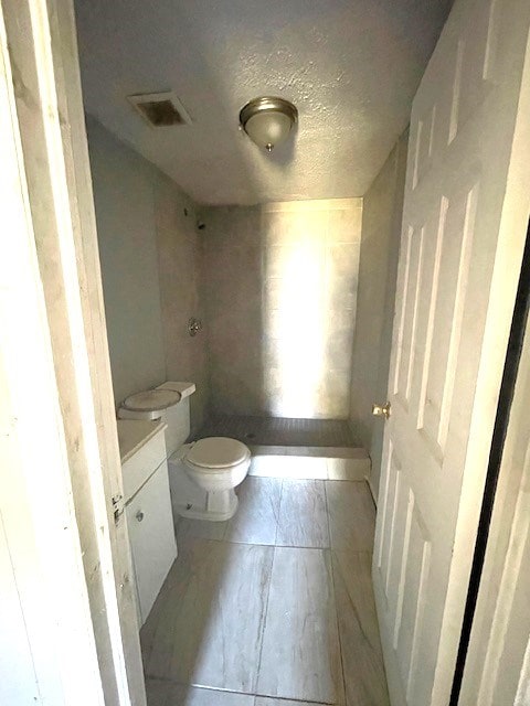 bathroom featuring a shower, a textured ceiling, vanity, and toilet