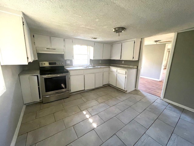 kitchen with stainless steel electric stove, sink, white cabinets, and a textured ceiling