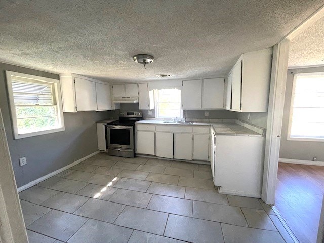 kitchen featuring a healthy amount of sunlight, a textured ceiling, white cabinetry, and stainless steel range with electric cooktop