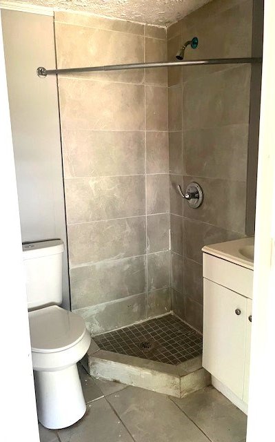 bathroom with tiled shower, tile patterned floors, vanity, and toilet