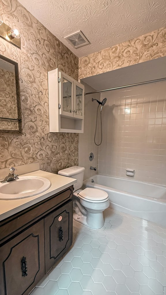 full bathroom featuring tile patterned flooring, vanity, a textured ceiling, toilet, and tiled shower / bath