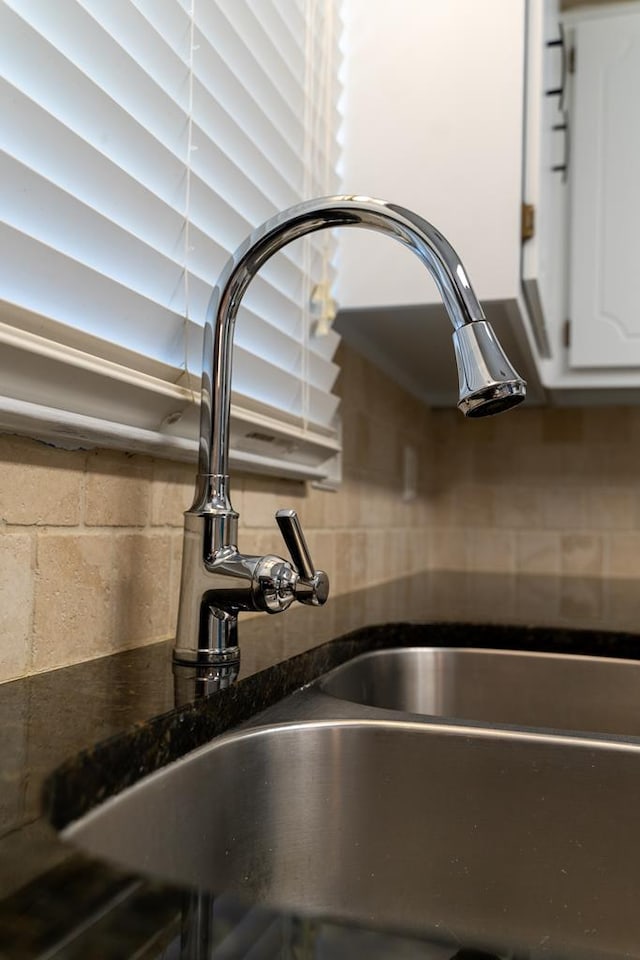 room details featuring white cabinetry, sink, decorative backsplash, and dark stone counters