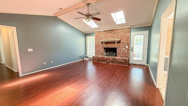 unfurnished living room featuring vaulted ceiling with skylight, hardwood / wood-style floors, ornamental molding, ceiling fan, and a brick fireplace