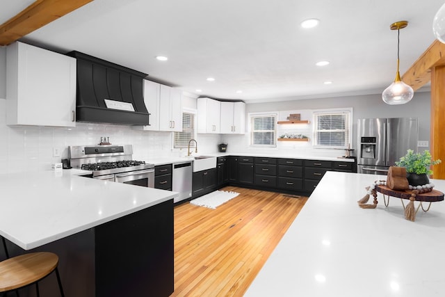 kitchen with kitchen peninsula, custom exhaust hood, stainless steel appliances, decorative light fixtures, and white cabinetry