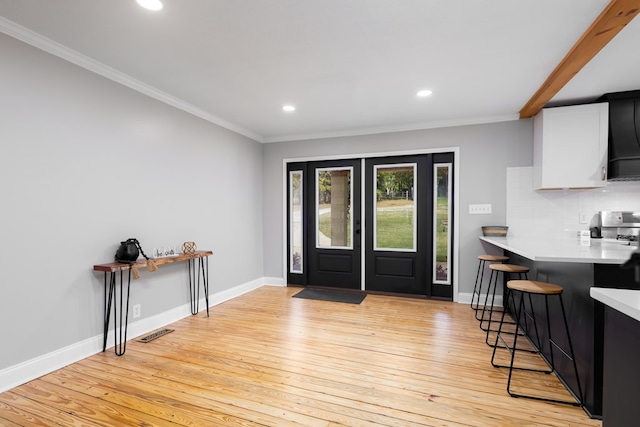 interior space featuring beam ceiling, ornamental molding, and light hardwood / wood-style flooring