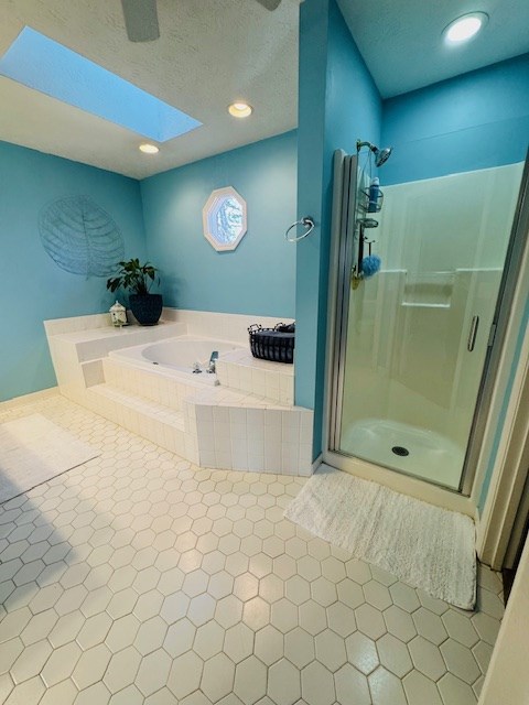 bathroom with tile patterned flooring, a skylight, plus walk in shower, and a textured ceiling