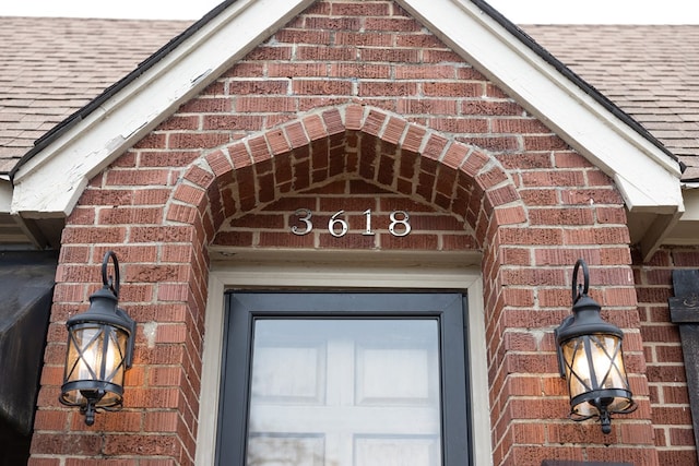 exterior details featuring a shingled roof and brick siding