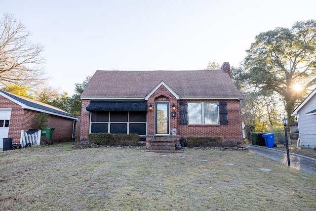 view of front of house with a shingled roof, a front lawn, and brick siding