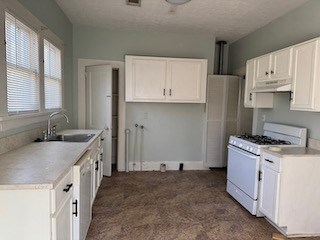 kitchen featuring white gas stove, light countertops, white cabinetry, a sink, and under cabinet range hood