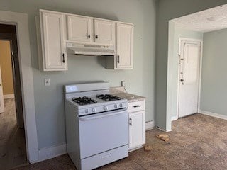 kitchen with white cabinetry, white gas stove, under cabinet range hood, and baseboards