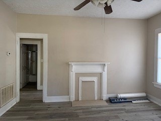 unfurnished living room with a ceiling fan, a textured ceiling, baseboards, and wood finished floors