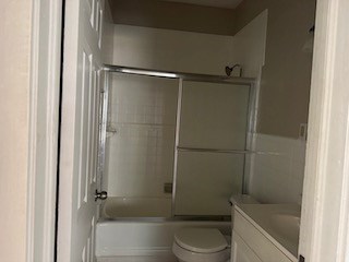 full bath with toilet, shower / bath combination with glass door, and vanity