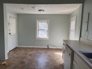 unfurnished dining area featuring a textured ceiling, a sink, and baseboards