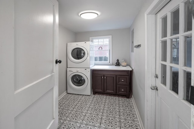 laundry room featuring cabinet space, baseboards, light tile patterned floors, and stacked washer and clothes dryer