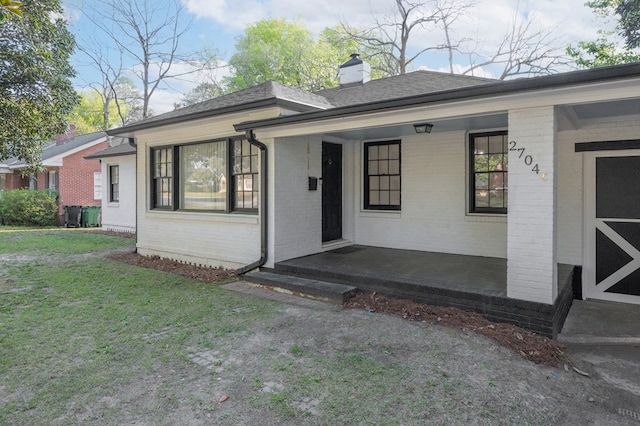 view of front of house featuring a porch, brick siding, a chimney, and a front lawn