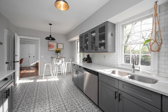 kitchen featuring a sink, dishwasher, decorative backsplash, gray cabinetry, and glass insert cabinets