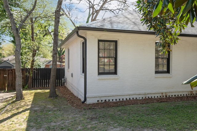 view of property exterior with brick siding, fence, and a shingled roof