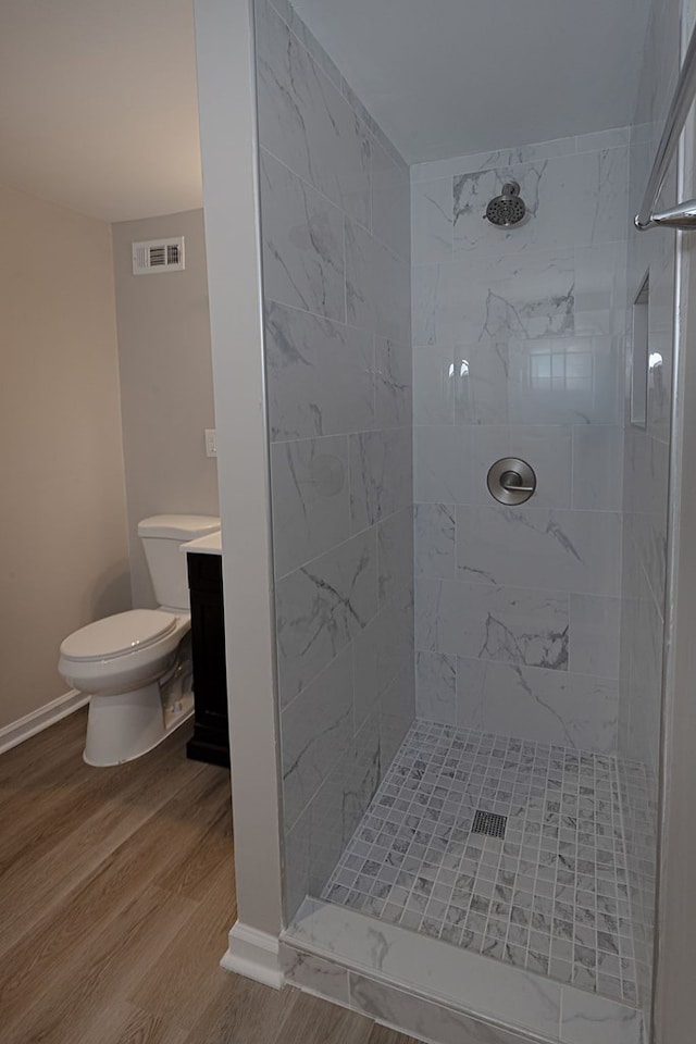 bathroom with a tile shower, hardwood / wood-style floors, vanity, and toilet