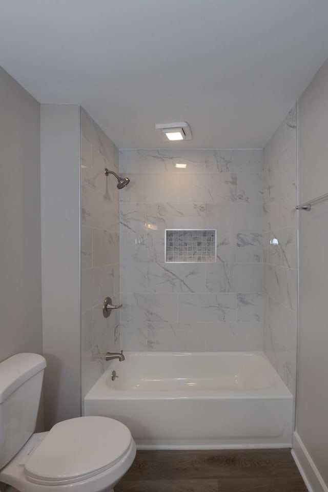 bathroom with wood-type flooring, tiled shower / bath combo, and toilet