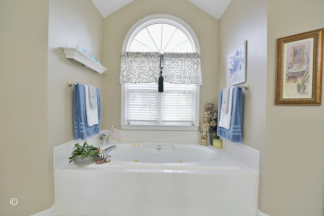 bathroom with a healthy amount of sunlight, tiled bath, and vaulted ceiling