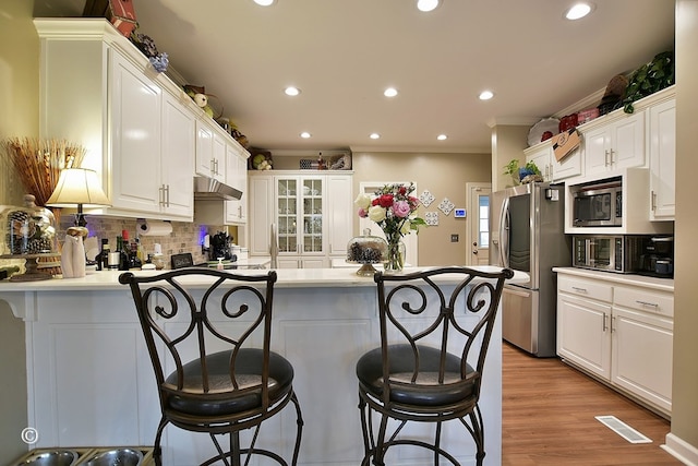 kitchen featuring a kitchen bar, white cabinets, stainless steel appliances, and ornamental molding