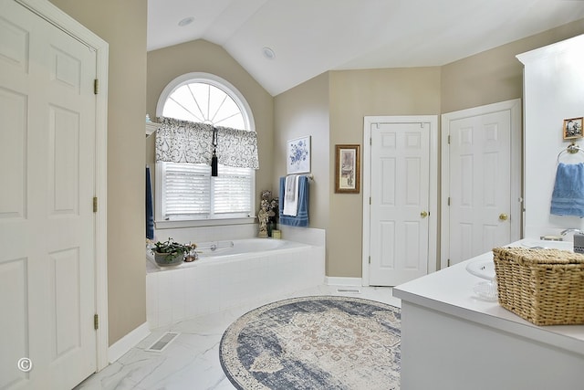 bathroom featuring vanity, a relaxing tiled tub, and lofted ceiling