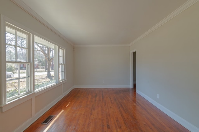empty room with baseboards, wood finished floors, visible vents, and ornamental molding