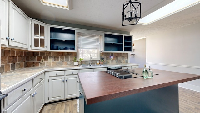 kitchen with a kitchen island, a sink, white cabinets, light countertops, and decorative backsplash