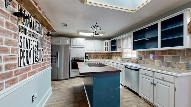 kitchen with a center island, hanging light fixtures, black appliances, white cabinetry, and a sink