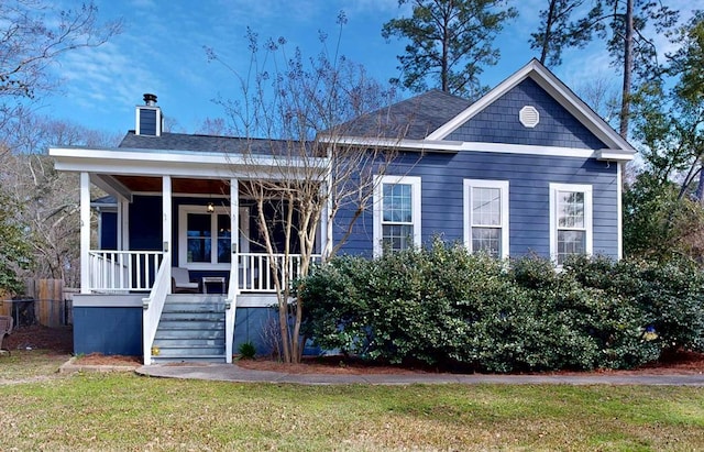 view of front of house featuring covered porch, a shingled roof, a chimney, and a front lawn