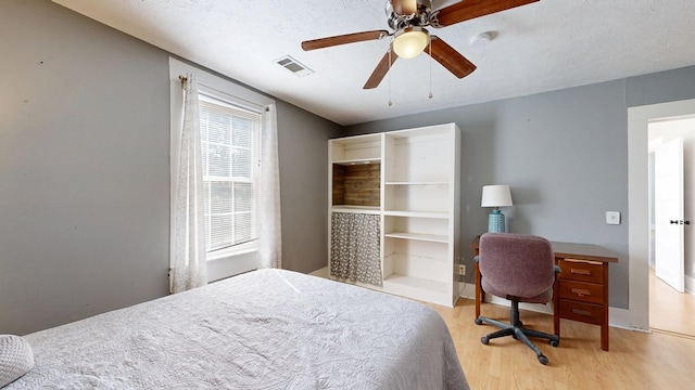 bedroom featuring light wood finished floors, ceiling fan, visible vents, and a textured ceiling