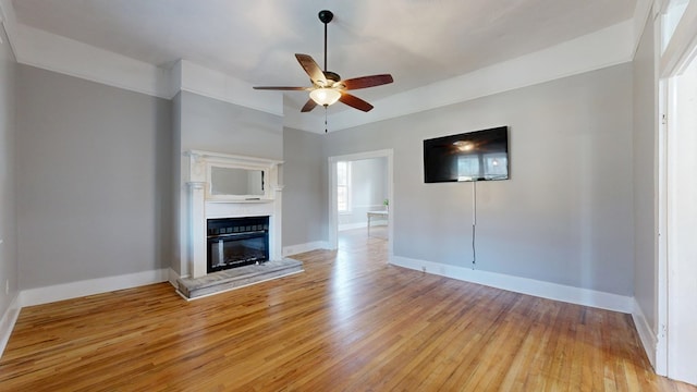 unfurnished living room featuring light wood-type flooring, ceiling fan, baseboards, and a glass covered fireplace