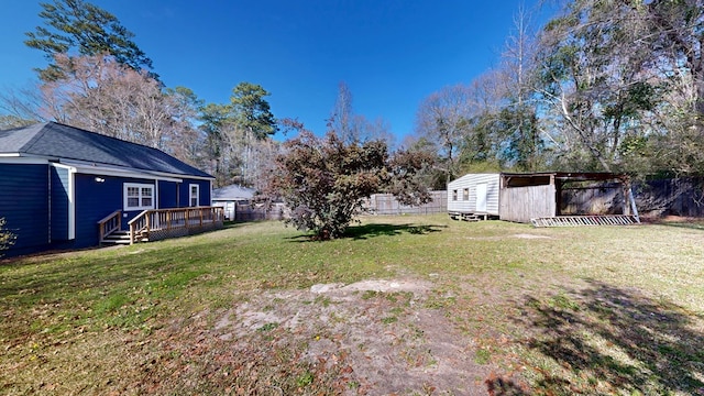 view of yard featuring an outbuilding, fence, a wooden deck, and a storage shed