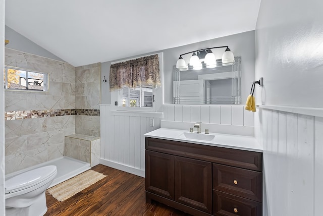 bathroom featuring a tile shower, hardwood / wood-style floors, vaulted ceiling, toilet, and vanity