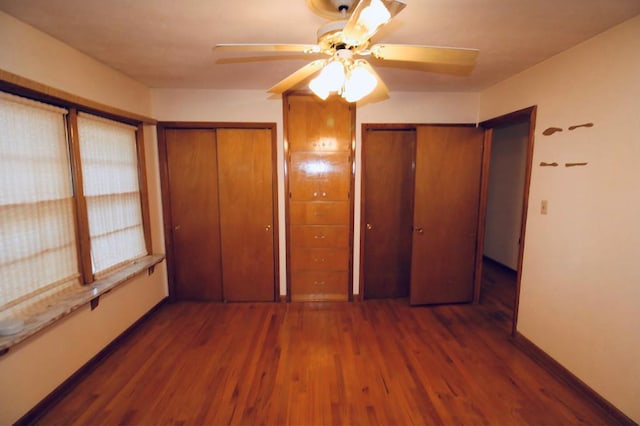 unfurnished bedroom featuring ceiling fan, dark hardwood / wood-style floors, and two closets