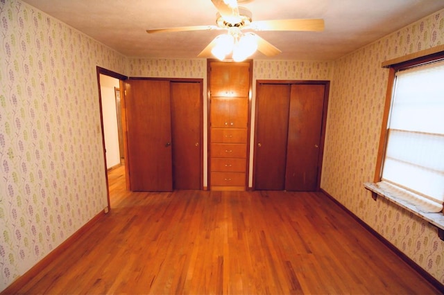 unfurnished bedroom featuring ceiling fan, two closets, and hardwood / wood-style floors