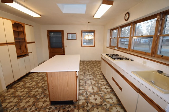 kitchen with stainless steel gas stovetop, a center island, sink, white cabinets, and pendant lighting