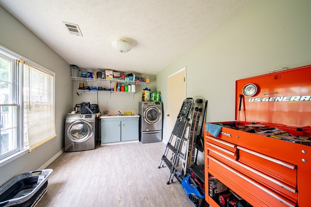 laundry area featuring visible vents, washing machine and dryer, light wood-style floors, a textured ceiling, and a sink