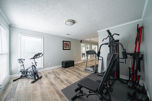 exercise area featuring crown molding, a textured ceiling, light wood finished floors, and baseboards