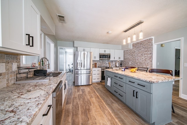 kitchen featuring visible vents, decorative backsplash, white cabinetry, light wood-style flooring, and stainless steel appliances