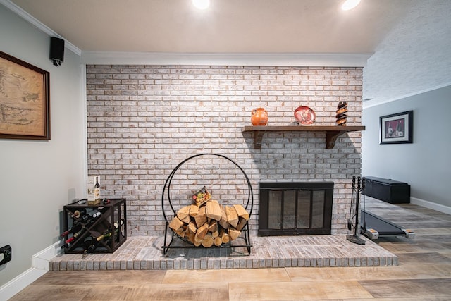 details featuring a brick fireplace, a textured ceiling, baseboards, wood finished floors, and ornamental molding