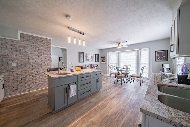 kitchen featuring a ceiling fan, wood finished floors, brick wall, gray cabinets, and a sink