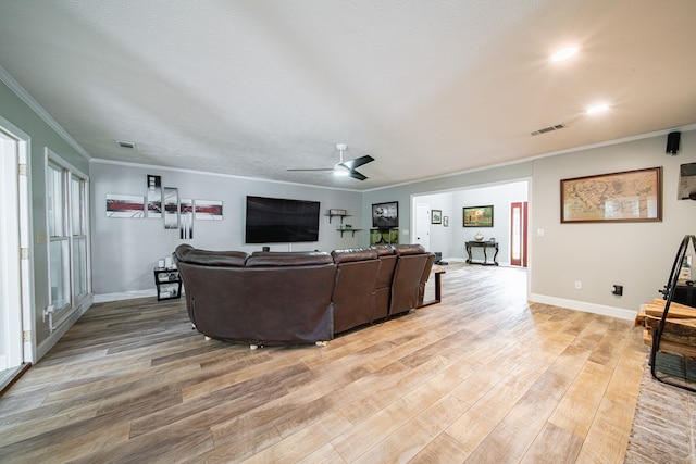 living room featuring crown molding, light wood-style flooring, a ceiling fan, baseboards, and visible vents