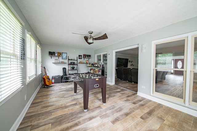 rec room featuring a textured ceiling, baseboards, and light wood-type flooring