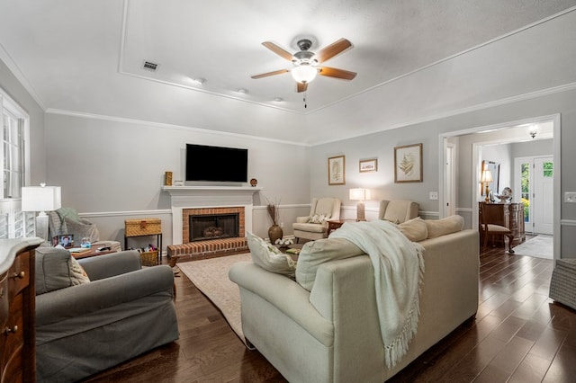 living area with a tray ceiling, ceiling fan, dark wood-style floors, a brick fireplace, and ornamental molding
