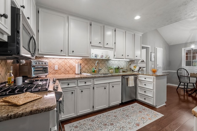 kitchen with appliances with stainless steel finishes, a sink, a peninsula, white cabinets, and vaulted ceiling