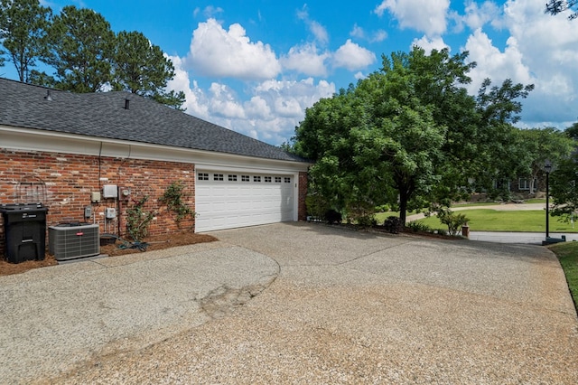 view of side of property featuring central air condition unit, concrete driveway, an attached garage, roof with shingles, and brick siding