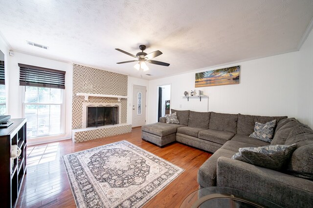 5728 Lexington Dr, Columbus, GA 31907 - living room featuring ceiling fan, wood finished floors, a tile fireplace, a textured ceiling, and ornamental molding